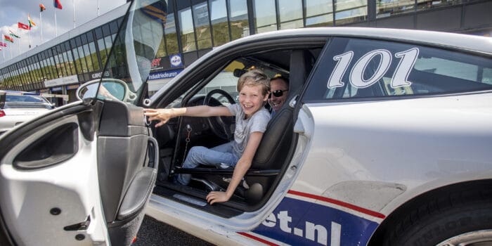 Jongen zit met grote glimlach achter het stuur van een Porsche 911 op Circuit Zandvoort tijdens het autorijden voor de jeugd.